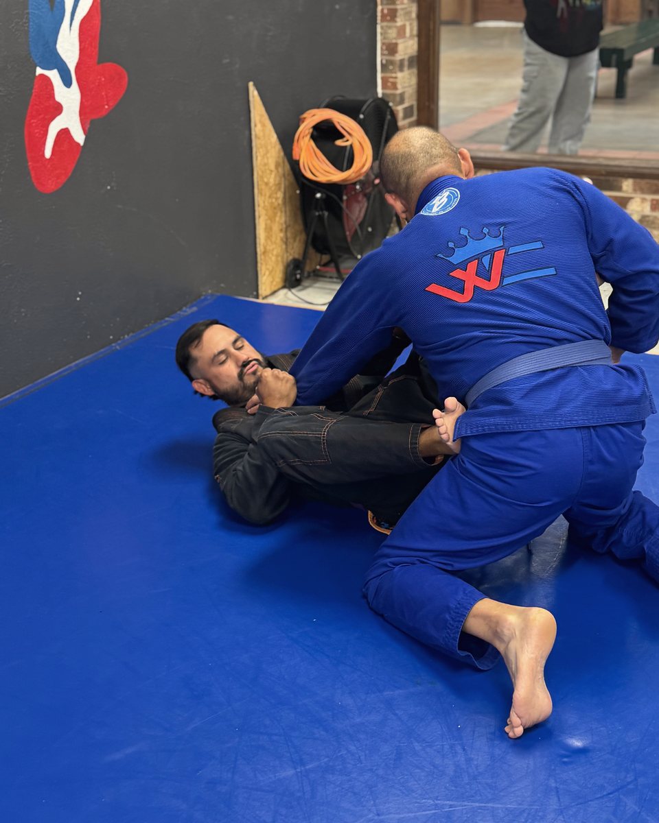 Two adults in blue and black gis practicing together on blue mats.
